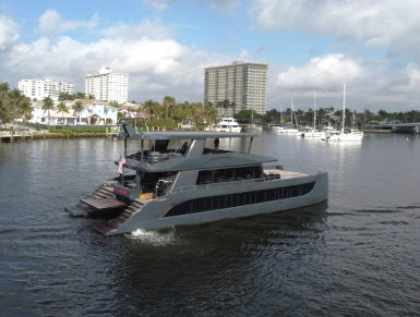 A picture of a grey 25-metre yacht in the water with a marina and apartment blocks in the background.